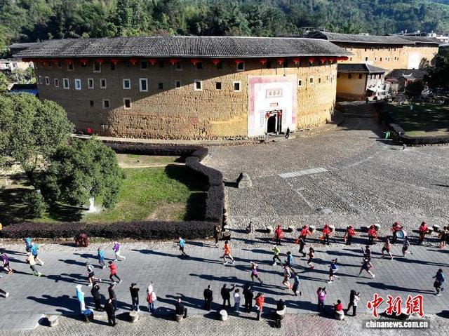 图为参赛选手从“福建土楼王”承启楼前经过。(无人机照片)中新社记者 张斌 摄