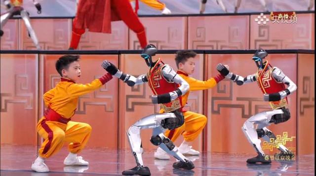 由宇树科技机器人与河南塔沟武术学校的小朋友同台呈现的节目《武BOT》中，机器人在和小朋友对练。(央视频截图)