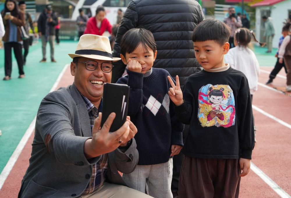 11月4日，一名印度尼西亚农村干部研修班学员在参观南山幼儿园时与小朋友合影。新华社记者 徐速绘 摄