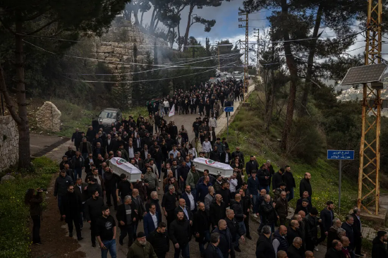 大批哀悼者聚集，部分人抬着两具覆盖着旗帜的白色棺椁