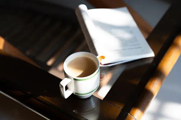 室内木质桌面上的咖啡杯与翻开书本。图源：视觉中国