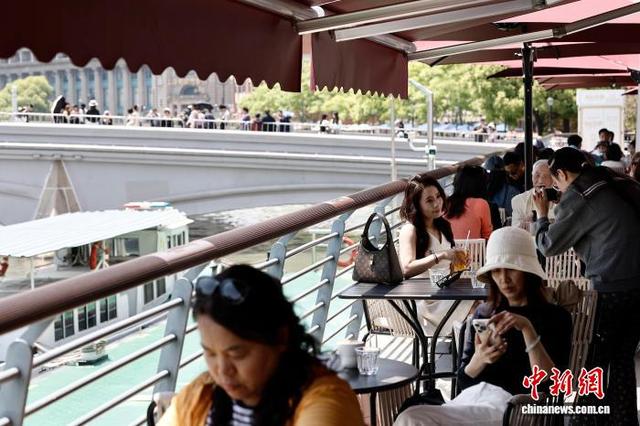 5月1日，游客在上海市虹口区北苏州河路某餐厅外一边品尝美食、一边拍照，享受“五一”假期户外生活。中新社记者 殷立勤 摄