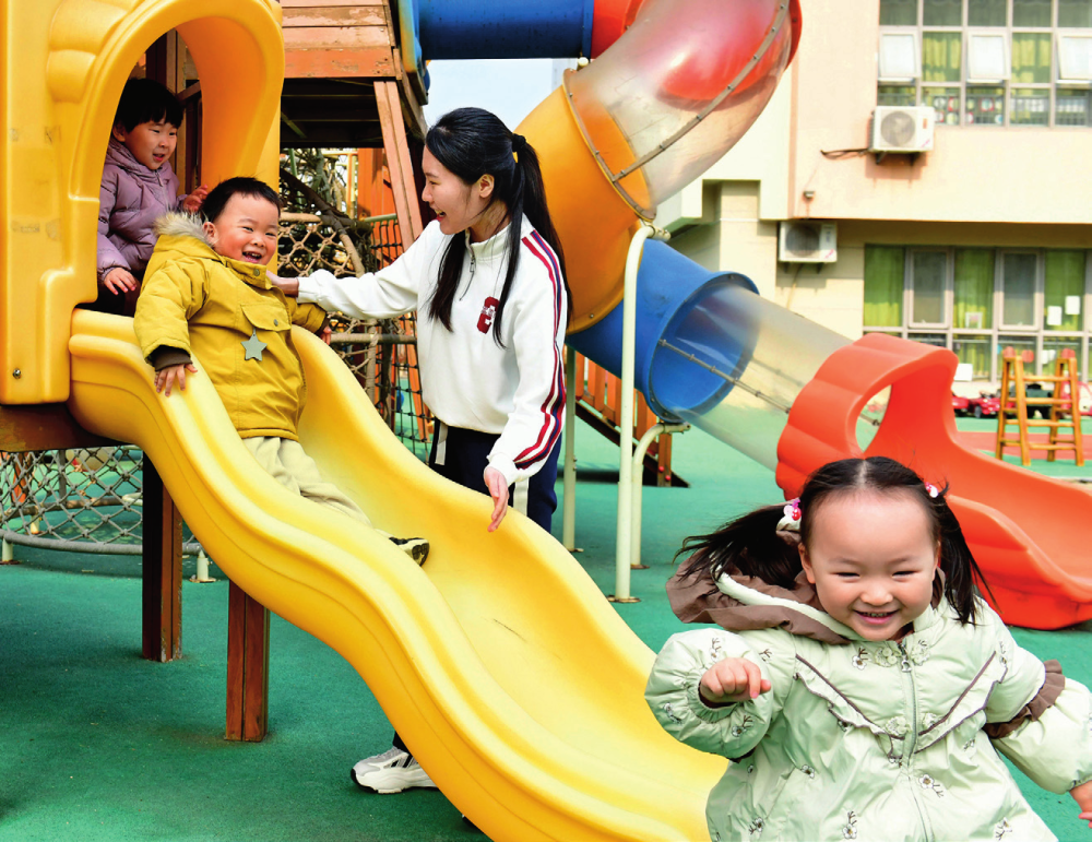 在山东省日照市市直机关幼儿园，老师在陪伴孩子们滑滑梯 （2025 年 2 月 20 日摄） 郭绪雷摄 / 本刊