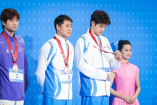 颁奖仪式上，潘展乐端详着自己的铜牌，他对奖牌的颜色似乎并不满意（本报记者王竟成摄）