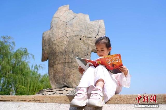 图为小朋友在甲骨雕塑前阅读刚刚发行的“跟着考古队长探秘殷墟”系列绘本。中新社记者 李超庆 摄