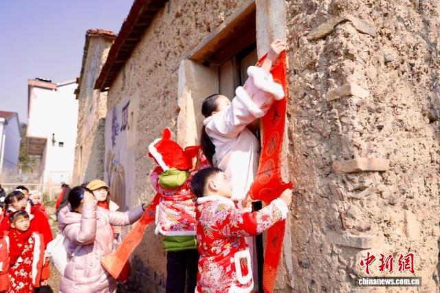 2月8日，浙江嵊州，学子们在泥砖房门前张贴春联。中新社记者 肖健 摄