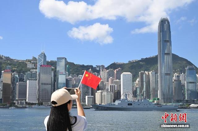 图为一位女士手持五星红旗在尖沙咀码头拍摄海军沂蒙山舰。 中新社记者 李志华 摄